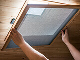 A man installing a screen on a window located on the ceiling.