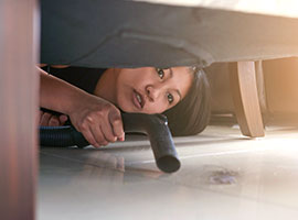 A woman bent down vacuuming underneath her sofa.