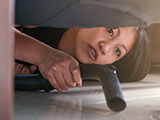 A woman bent down vacuuming underneath her sofa.