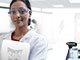 A smiling entomologist, wearing a lab coat and glasses, standing in a lab of the SC Johnson® Institute of Insect Science for Family Health