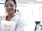 A smiling entomologist, wearing a lab coat and glasses, standing in a lab of the SC Johnson® Institute of Insect Science for Family Health