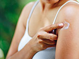 A young woman applying an anti-itch lotion to a mosquito bite on her arm.