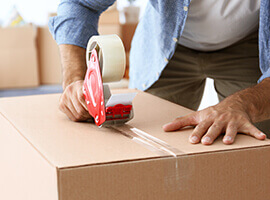 A man sealing a cardboard box with tape.