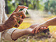 A mom spraying insect repellent on a child's arm outside.