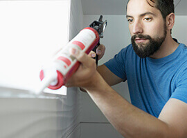 A man caulking an indoor window.