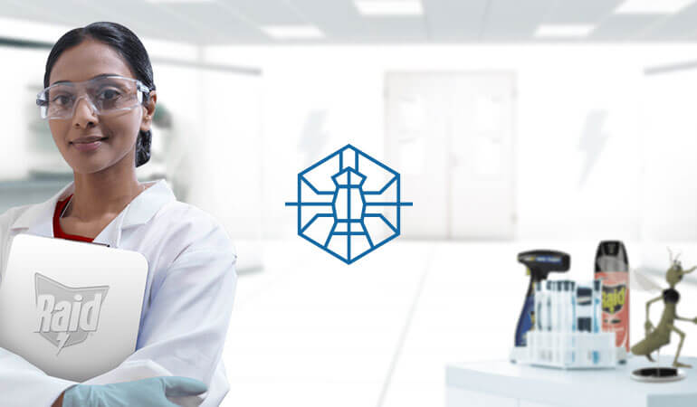 A smiling entomologist, wearing a lab coat and glasses, standing in a lab of the SC Johnson® Institute of Insect Science for Family Health